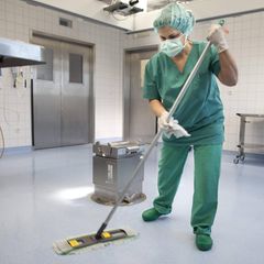 Eine Frau wischt einen OP-Saal, mit Haarnetz, Mundschutz und Handschuhen; Symbolbild Reinigungskraft OP