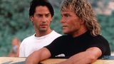 Keanu Reeves neben Patrick Swayze, der sich auf ein Surfbrett stützt