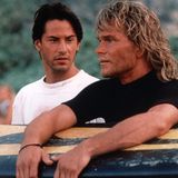 Keanu Reeves neben Patrick Swayze, der sich auf ein Surfbrett stützt