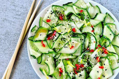 Ein asiatischer Gurkensalat in einer weißen Porzellanschale mit hellen Essstäbchen links daneben