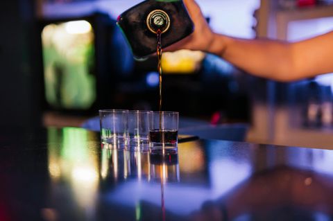 Symbolbild "Alkohol ab 18?"Jemand schenkt aus einer Flasche braune Flüssigkeit in drei Schnapsgläser