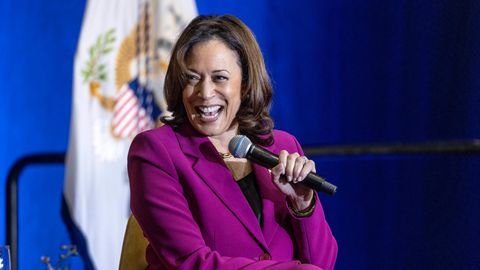 Kamala Harris sitzt auf einer Bühne und lacht, während sie mit links ein Mikro hält