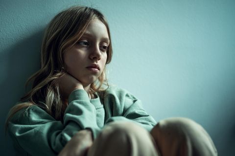 Ein junges Mädchen mit Depressionen sitzt traurig an eine Wand gelehnt