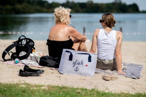 Zwei Frauen sitzen bei Sommer-Wetter und hohen Temperaturen im Sand an einem See