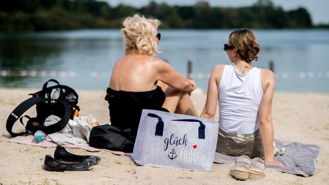 Zwei Frauen sitzen bei Sommer-Wetter und hohen Temperaturen im Sand an einem See