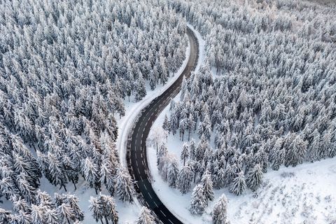 Wetter im Winter: Luftaufnahme von verschneitem Nadelwald, durch den sich eine Straße schlängelt