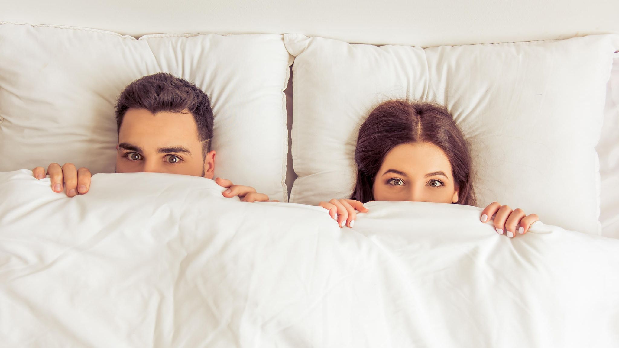 Schmerzen beim Sex: Ein Paar liegt mit aufgerissenen Augen unter der Bettdecke