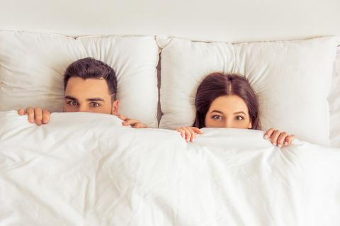Schmerzen beim Sex: Ein Paar liegt mit aufgerissenen Augen unter der Bettdecke