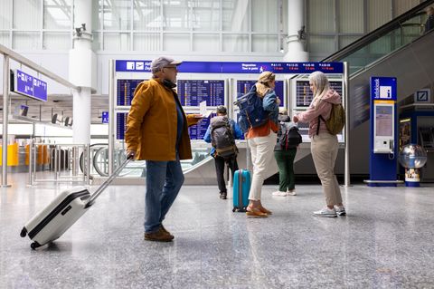 Großaufnahme von Reisenden, die auf dem Flughafen vor den Abflugtafeln stehen und herumlaufen.