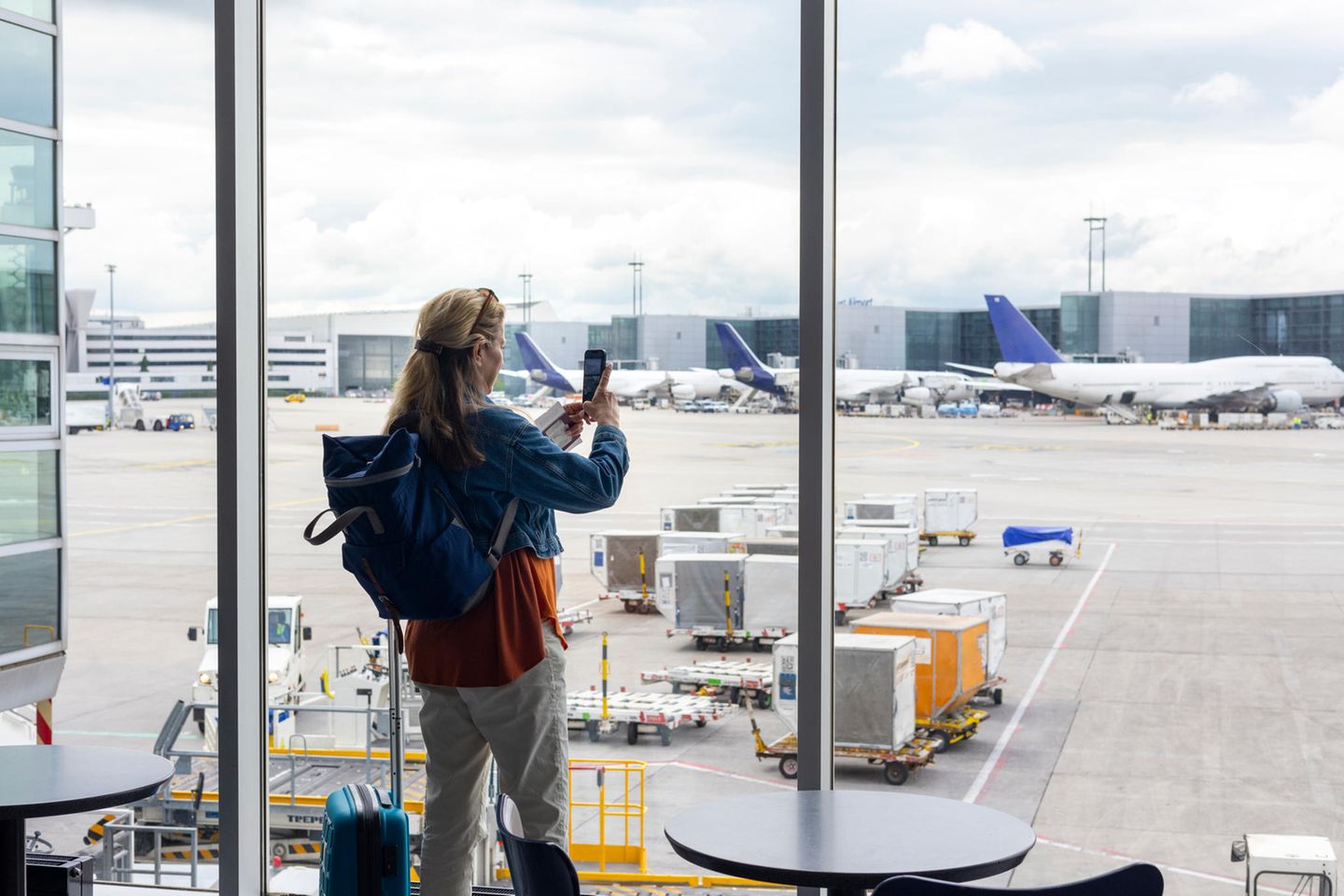 Weitwinkelaufnahme einer Frau auf einem Flughafen. Sie hält ihr Mobiltelefon in der Hand, um Fotos von den Flugzeugen zu machen.