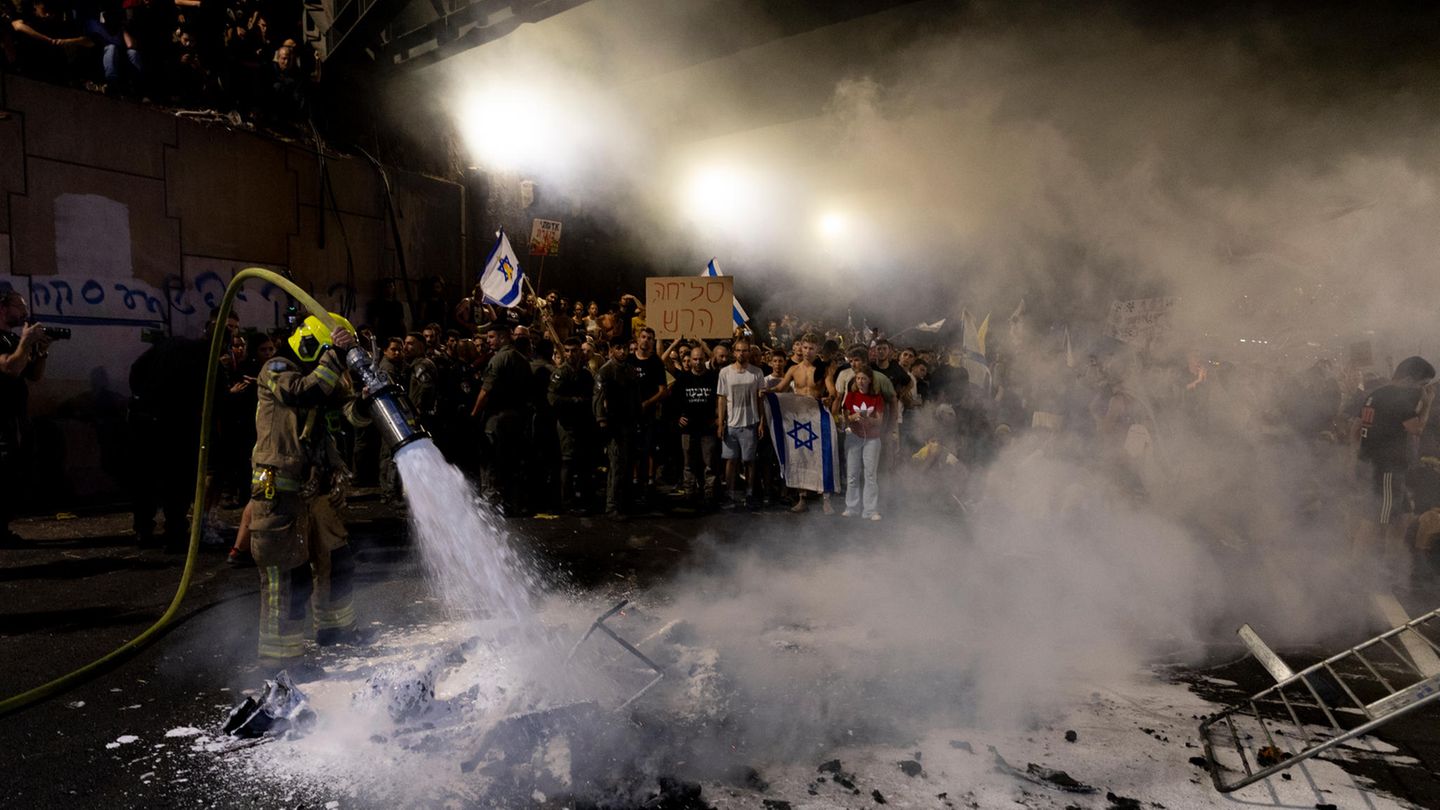 Ein Feuerwehrmann löscht ein Feuer, das Demonstrierende entfacht hatten. Tagsüber hatten bereits die Beschäftigten vieler Organisationen und Behörden gestreikt – aus Protest gegen den schleppenden Verlauf der Verhandlungen über die Freilassung der noch immer gut 100 im Gazastreifen vermuteten Geiseln, bei denen unklar ist, wie viele von ihnen überhaupt noch leben