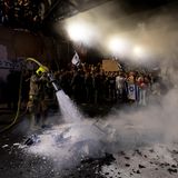 Ein Feuerwehrmann löscht ein Feuer, das Demonstrierende entfacht hatten. Tagsüber hatten bereits die Beschäftigten vieler Organisationen und Behörden gestreikt – aus Protest gegen den schleppenden Verlauf der Verhandlungen über die Freilassung der noch immer gut 100 im Gazastreifen vermuteten Geiseln, bei denen unklar ist, wie viele von ihnen überhaupt noch leben