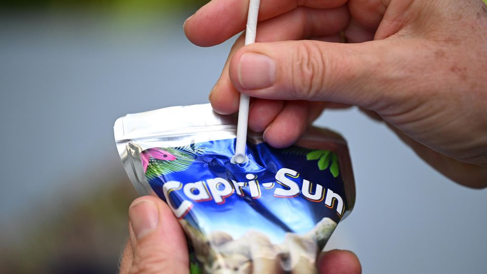 Ein Mann versucht, einen Pappstrohhalm in eine Tüte Capri Sun zu stechen