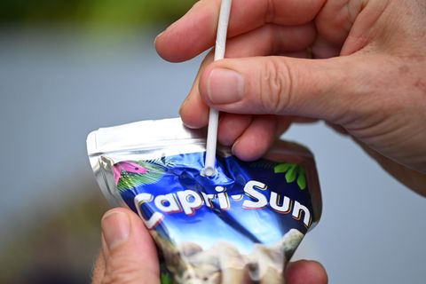 Ein Mann versucht, einen Pappstrohhalm in eine Tüte Capri Sun zu stechen