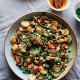 Verenas Kartoffelsalat  Verena ist in Deutschland aufgewachsen, und sie erinnert sich noch  daran, dass es in Sachen Kartoffelsalat zwei Fraktionen gibt: die Mayo-  Fans und die Fraktion Brühe-Öl. Dies ist eine Brühe-Öl-Version, wie  sie in Süddeutschland, besonders in Schwaben und Bayern, beliebt ist.  Sie ist weniger schwer und klumpig als die Mayo-Variante und verdankt  ihre Cremigkeit der Stärke aus den Kartoffeln. Sie tritt während  der 2 Stunden aus, die sie in der warmen Brühe verbringen. Wir haben  uns über die Tradition hinweggesetzt und etwas Pancetta hinzugefügt  (warum auch nicht?); für extra Frische auch noch fein gewürfelte Gurke.     Zutaten:  500 g festkochende Kartoffeln  75 ml Olivenöl  1 kleine Zwiebel, fein gehackt (125 g)  1 Knoblauchzehe, geschält und zerdrückt  175 ml Hühnerbrühe  2 TL Dijonsenf  2 EL Apfelessig  ½ TL schwarze Pfefferkörner, im Mörser grob zerstoßen  15 g Schnittlauch, 10 g in Röllchen geschnitten, 5 g in 1,5 cm lange Stücke geschnitten  1 Pck. geräucherte Pancetta, fein gewürfelt (75 g)  1 TL Paprikapulver  ¼ Gurke, längs halbiert und entkernt und in 5 mm große Würfel geschnitten (100 g)  Salz     Zubereitung:  Für 4 Personen  Die Kartoffeln in einem Topf, für den ein passender Deckel vorhanden  ist, knapp mit Wasser bedecken und großzügig salzen. Bei mittlerer bis  starker Hitze zum Kochen bringen, dann bei mittlerer bis schwacher  Hitze zugedeckt 20–25 Minuten garen, bis die Kartoffeln gerade eben  weich sind. Abgießen und, sobald sie so weit abgekühlt sind, dass man  sie anfassen kann, pellen und in 5 mm dicke Scheiben schneiden. In  einer Schüssel beiseitestellen.  In einer Pfanne mit hohem Rand 2 EL Öl bei mittlerer Temperatur er­hitzen.  Die Zwiebel darin unter regelmäßigem Rühren 12–15 Minuten  anschwitzen, bis sie karamellisiert ist. Knoblauch und Brühe darin  zum Köcheln bringen, dann vom Herd nehmen. Senf, Essig, 1¼ TL Salz,  Pfeffer und 2 weitere EL Öl hinzufügen. Alles verquirlen, dann auf die  Kartoffeln gießen. Vorsichtig, aber gründlich durchheben: Die Mischung  sieht sehr nass aus (und einige Kartoffelscheiben werden zerbrechen),  aber das ist normal. Für 2 Stunden bei Zimmertemperatur beiseitestellen, damit die Kartoffeln etwa die Hälfte der Brühe aufsaugen können,  dann die Schnittlauchröllchen unterrühren.  Inzwischen die Pfanne auswischen und bei mittlerer bis hoher Temperatur erhitzen. Die Pancetta darin bei mittlerer bis schwacher Hitze  10–12 Minuten braten, bis die Würfel knusprig sind; ab und zu um­rühren.  Mit einem Schaumlöffel auf einen mit Küchenpapier belegten  Teller heben – etwa 1 EL Fett in der Pfanne lassen – und beiseitestellen.  Sobald sie kalt ist, die Pancetta zu feinen Bröseln hacken.  Den restlichen EL Öl mit Paprikapulver zum Fett in der Pfanne mischen.  Ungefähr 30 Sekunden rühren, bis es duftet, dann vom Herd nehmen.  Wenn serviert werden kann, die Gurkenwürfel unter den Salat heben,  den Salat auf einer Servierplatte anrichten. Mit Pancettabröseln und  Schnittlauchstücken bestreuen, mit Paprikaöl beträufeln und servieren.