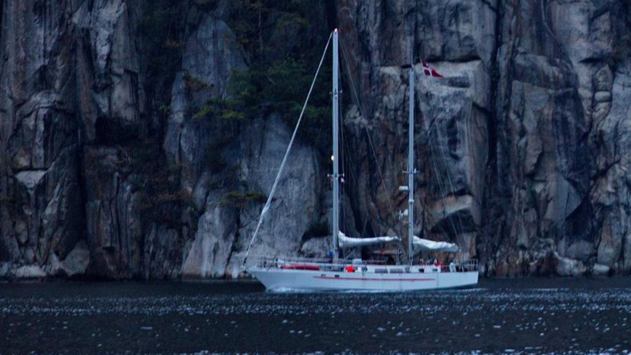Segelboot vor Steilküste, im Wasser schwimmt eine rote Boje