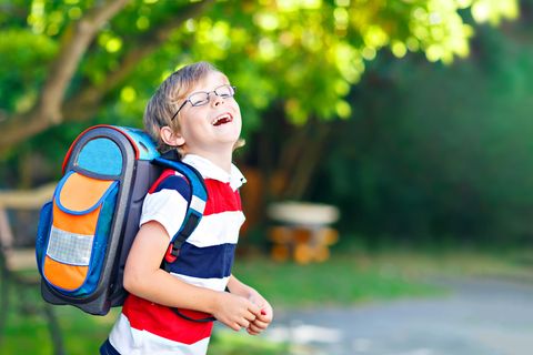 Ein Junge mit einem Schulrucksack lacht an einem sonnigen Tag verschmitzt in die Kamera