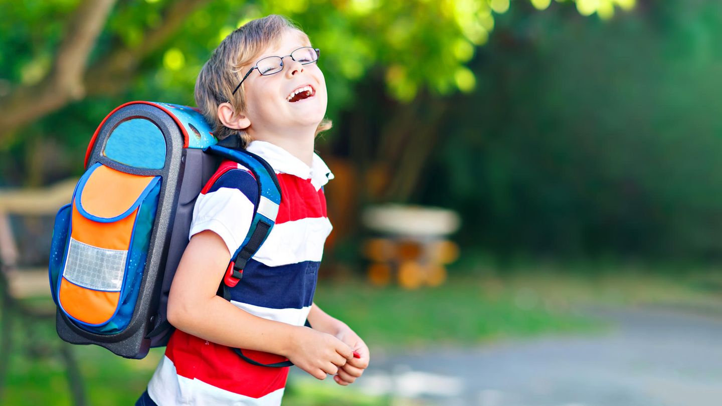 Ein Junge mit einem Schulrucksack lacht an einem sonnigen Tag verschmitzt in die Kamera