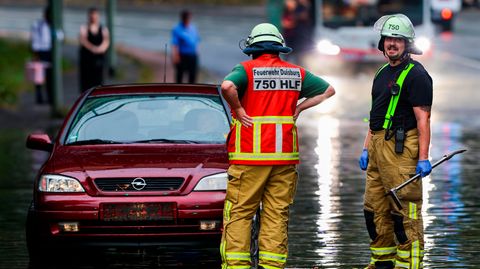 Zei Feuerwehrleute stehen in einer überschemmten Straße neben einem Auto