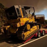 Von einem Tieflader entlädt die Feuerwehr eine Kettenraupe. Mit schwerem Gerät sollen Schneisen geschaffen werden, um das Airport Fire einzudämmen