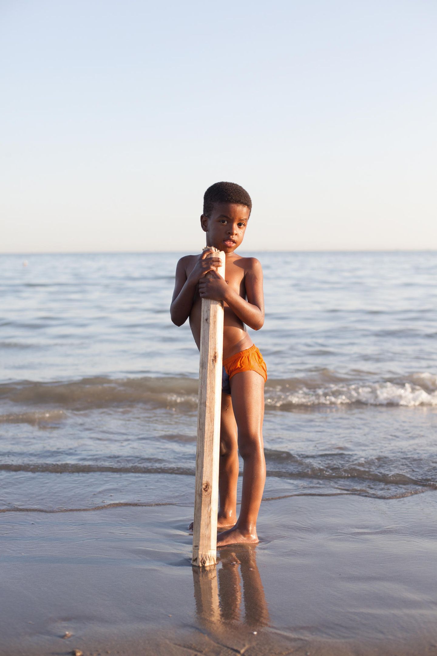 Ein Junge (Afro-Iraner) stützt sich auf ein Balken udn steht am Strand. Ein Junge (Afro-Iraner) stützt sich auf ein Balken udn steht am Strand.
