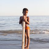 Ein Junge (Afro-Iraner) stützt sich auf ein Balken udn steht am Strand.