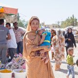 Eine junge, selbstbewusste Frau (Afro-Iranerin) hält ein schlafendes Baby im Arm.