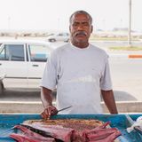 Ein Afro-Iraner mit Schnauzbart steht mit dem Rücken zur Straße und verkauft Fisch.