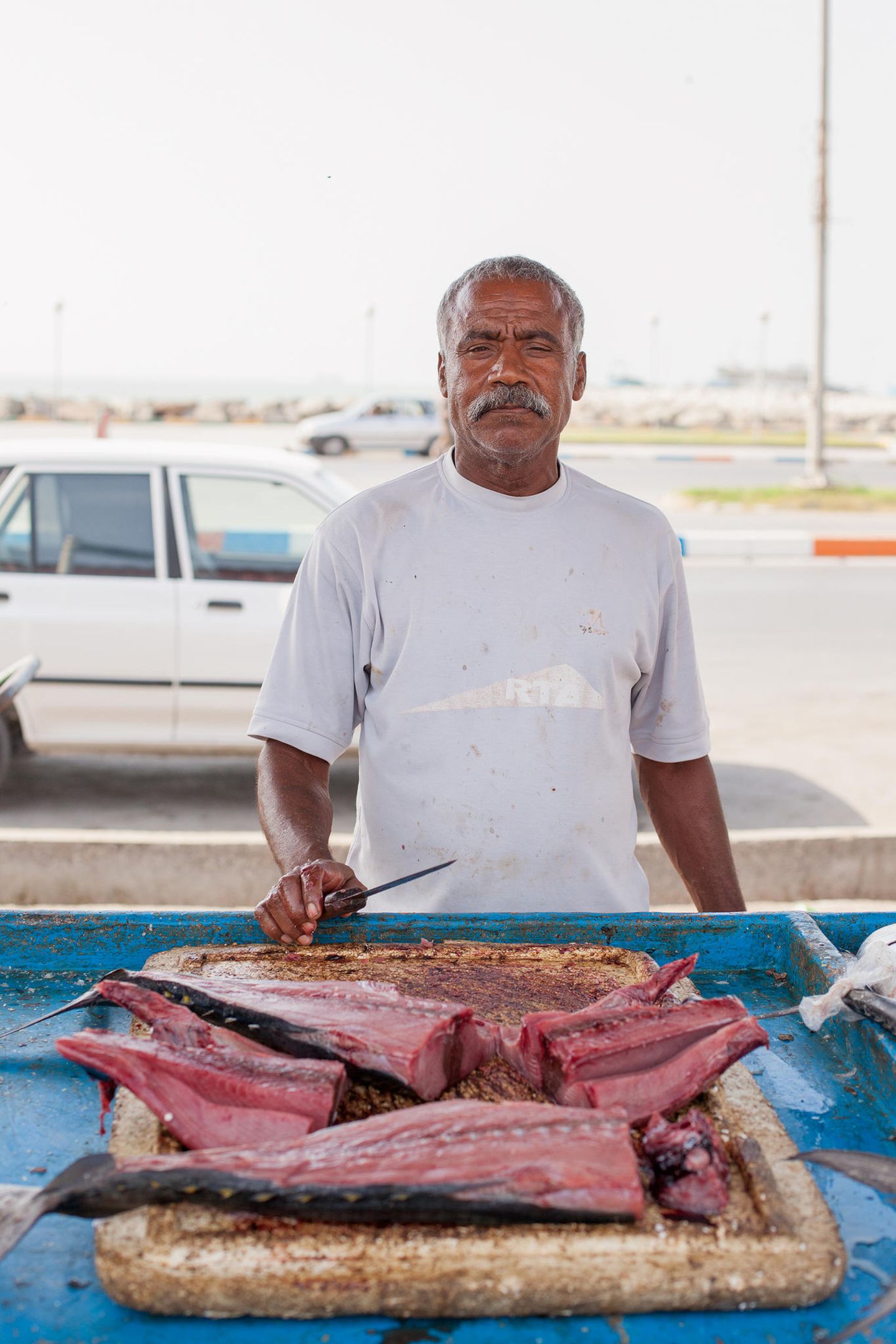 Ein Afro-Iraner mit Schnauzbart steht mit dem Rücken zur Straße und verkauft Fisch.
