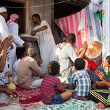 Eine Gruppe von afro-iranischen Männern und Jungs sitzt zusammen auf dem Boden und trommelt und klatscht.