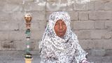 Eine afro-iranische Frau mit Kopftuch sitzt im Schneidersitz auf dem Boden.
