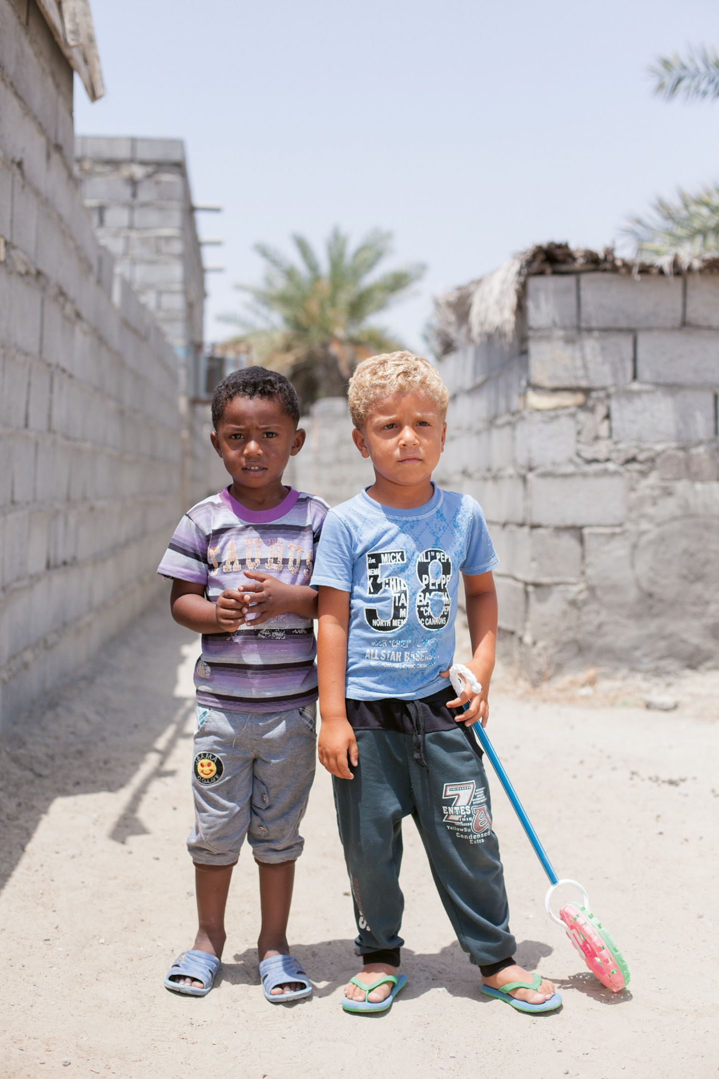 Zwei kleine Jungen (Afro-Iraner) im Kindergartenalter stehen vor unverputzen Wänden.