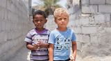 Zwei kleine Jungen (Afro-Iraner) im Kindergartenalter stehen vor unverputzen Wänden.