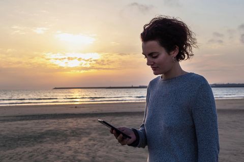 Frau schaut beim Online-Dating auf ihr Handy am Strand