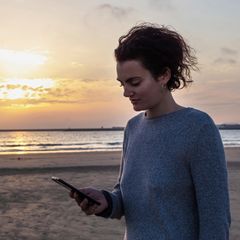 Frau schaut beim Online-Dating auf ihr Handy am Strand