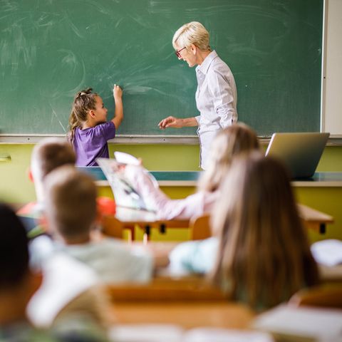 Lehrerin steht mit junger Schülerin an der Tafel