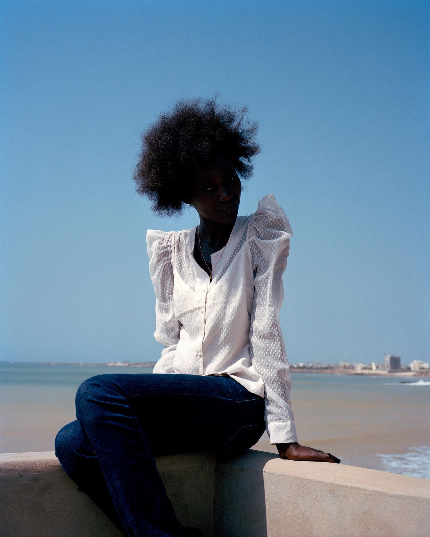 Eine Frau mit Afro sitzt vor einem strahlend blauen Himmel im Gegenlicht