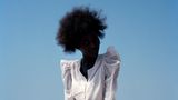 Eine Frau mit Afro sitzt vor einem strahlend blauen Himmel im Gegenlicht