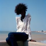 Eine Frau mit Afro sitzt vor einem strahlend blauen Himmel im Gegenlicht