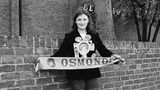 Ein kleines Mädchen dass ein Fan der Osmonds ist hält einen Fan Schal hoch
