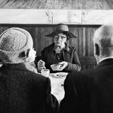 Eine Dame macht bei einem Buffet Sahne in ihren Kaffee, über ihr hängt eine Version des letzten Abendmahls