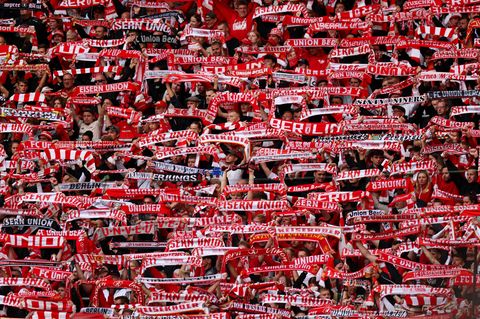 Fans von Union Berlin halten im Stadion ihre rot-weißen Schals hoch