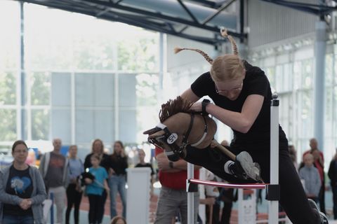 Hobby Horsing: Mädchen springt mit Steckenpferd über ein Hindernis