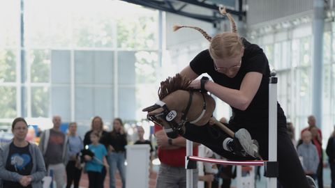 Hobby Horsing: Mädchen springt mit Steckenpferd über ein Hindernis