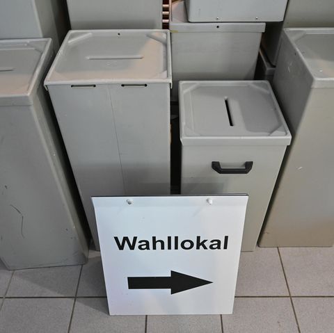 Leere Wahlurnen, davor ein Schild mit der Aufschrift Wahllokal und einem Pfeil nach rechts