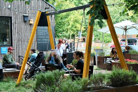 Menschen sitzen in einem Garten der Human Library und unterhalten sich. Zwei Frauen sitzen auf einer Schaukel