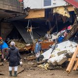 Menschen blicken auf Trümmer von Häusern