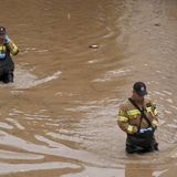 Menschen waten in wasserfester Kleidung durch schlammige Fluten