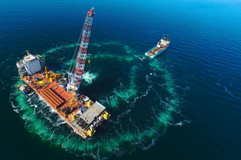 Beim Bau des Windparks "Hohe See" rammt ein Technikschiff (vorn) die Fundamente für Windrotoren in den Meeresgrund.