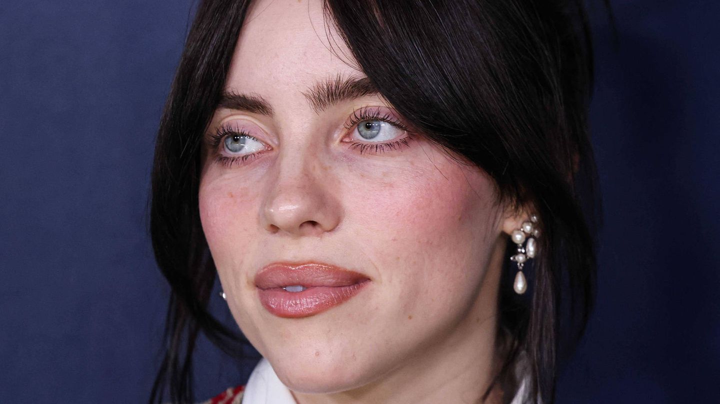 Billie Eilish mit hochgesteckten Haaren vor lila Hintergrund